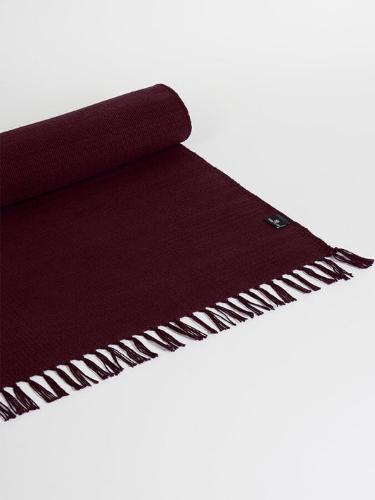 Burgundy woven blanket with fringes on a white background